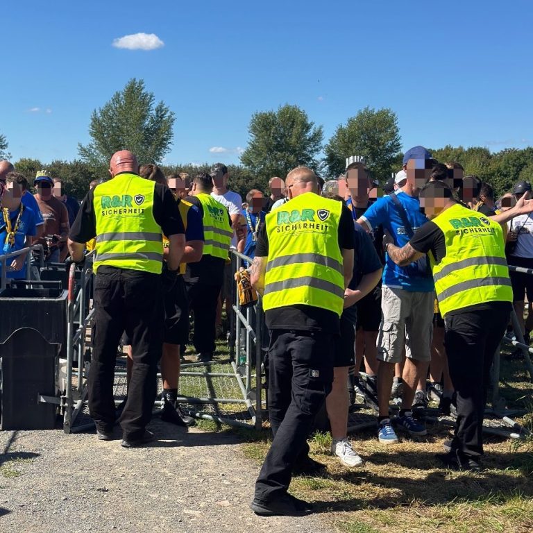 Sicherheitskräfte überprüfen Besucher an einem Veranstaltungseingang bei schönem Wetter.